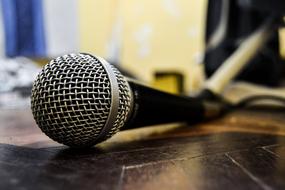 Close-up of the shiny, metallic and black microphone, on the wooden surface, in light and shadow