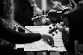 Black and white photo of the people, playing on the musical instruments, near the music sheet