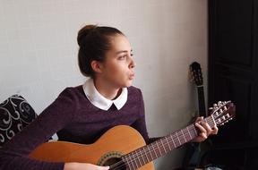 Profile portrait of a girl, playing on the wooden guitar and singing