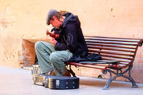 street musician on a bench with a guitar