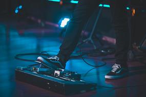 Man in "Vans" shoes using footswitch on the stage, with the lights