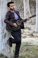 photo of a guitarist by a tree trunk