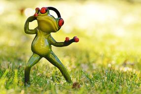 Cute, green and yellow frog figure with headphones, on the green grass