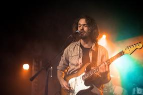 Concert of the young man with guitar on stage at colorful lights