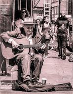 Retro photo of the street player in hat, playing on the guitar