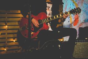 Person, playing on the beautiful, brown guitar, near the lights