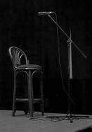 Black and white photo of a stage with the microphone and chair, among the darkness