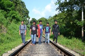 five young men walking on railroad through forest