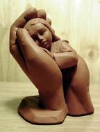 Beautiful, brown clay figure of the child in hand, on the wooden surface