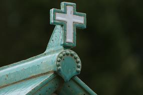 Aged turquoise and white Glaze ceramic Cross on rooftop