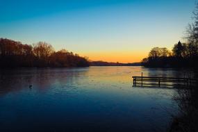 Beautiful landscape of the colorful lake, with the pier, among the trees, at colorful sunset on horizon