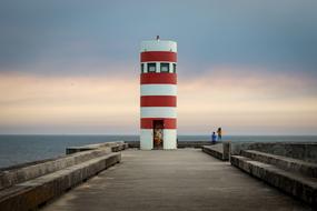 People near the beautiful, red and white lighthouse on the coast of Porto, Portugal at colorful sunset