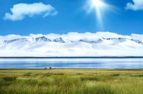 Green grass on the shore of the lake and snowy mountains
