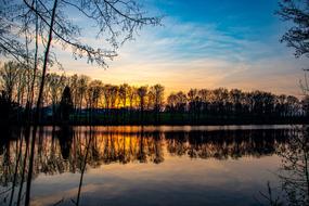 colorful Sunset Sky and bare trees mirroring on lake at dusk