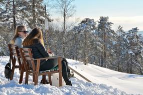 two girls are sitting on chairs in the winter forest