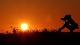 Silhouette of the girl taking photo at colorful sunset background
