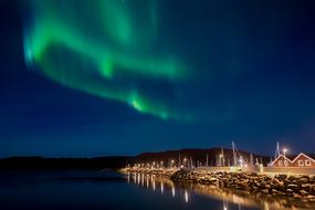 Beautiful green Northern Lights in deep blue sky above illuminated village in Norway