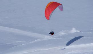 a man on a paraglider flies on a snowy mountain