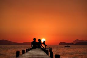 silhouette of Couple with dog on pier above sea at sunset