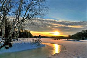 reflection of setting sun on river at forest on snowy winter