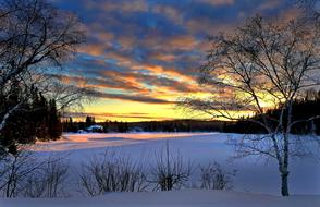 Beautiful landscape with the snowy field, among the trees and grass, at colorful sunset in Quebec, Canada