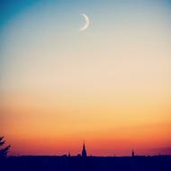 new Moon at colorful evening sky above old city