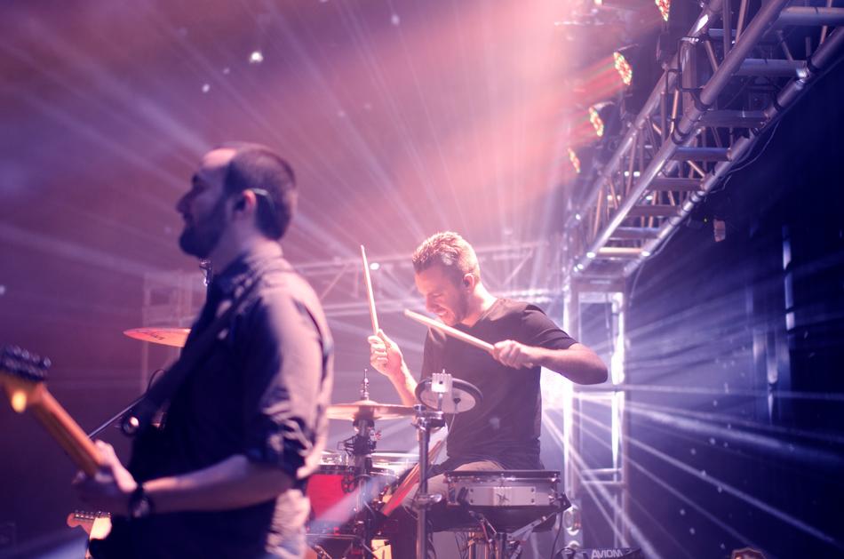 guitarist and drummer on stage under the rays of spotlights