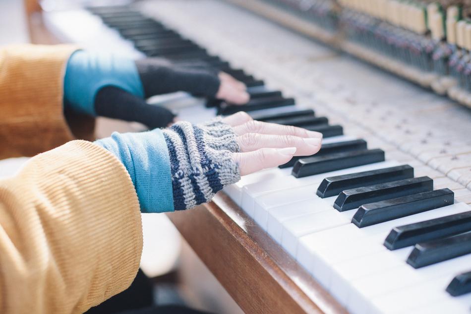 hands in braided gloves on piano keys in blurred background