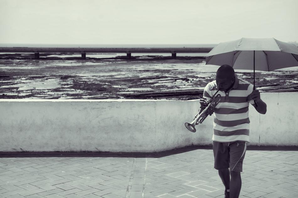 Black and white photo of a guy with umbrella, playing on the trumpet, on the beautiful shore in Panama