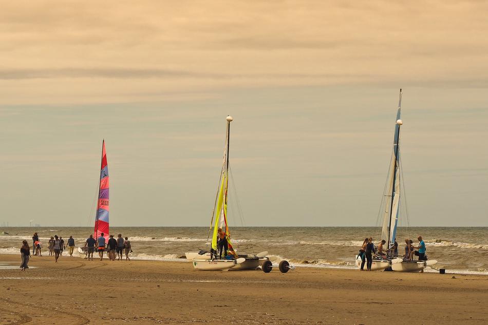 People near the colorful catamarans on the beautiful sandy beach at colorful sunset