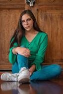 Young woman with glasses, sitting near the wooden wall