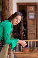 Young woman with glasses and in green clothing, posing near the fence