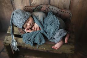 Cute, sleeping newborn child in the turquoise clothes, on the wooden surface