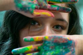 Girl, covering her face with hands with colorful paint