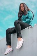 Beautiful girl, in turquoise jacket, sitting on the wall