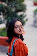 Portrait of the young, smiling girl in glasses, near the green plants
