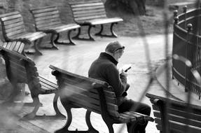 black and white photo of a man drinking a book on a park bench