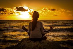 Back view of the girl, meditating on the beautiful shore, at colorful sunset on horizon