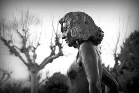 Black and white photo of the beautiful, shiny statue of the woman, among the trees