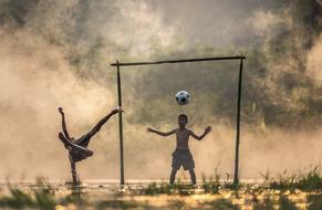 Children, playing football with the stick gates, among the mist, at colorful sunset, in Thailand