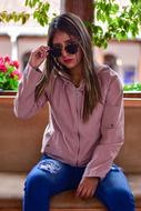 Young girl in pink sweatshirt, blue, ripped jeans and with sunglasses, sitting on the bench