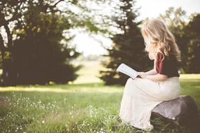 blonde girl reading a book on a meadow in a blurred background