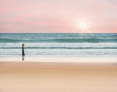 a lonely girl walks along the ocean on a background of pink sunset