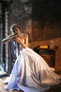 Beautiful Cinderella in white dress, sitting on the chair, in light