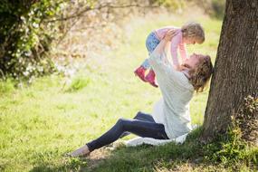 happy mom raises baby in her arms in the park