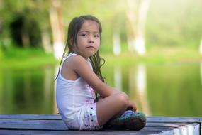 little asian girl sitting on a wooden pier by the lake