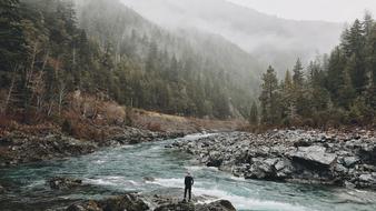 Person on the rock near the river, among the green trees in fog, on the mountains, on the beautiful landscape