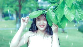 girl with black hair under the leaves of a tree during the rain