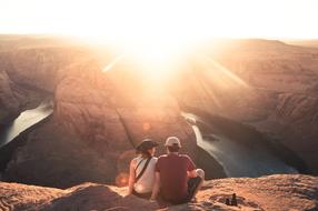 Back view of the couple in hats, sitting on the beautiful mountain in the canyon, in the colorful sunlight