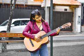 girl in a burgundy jacket plays the guitar on the street